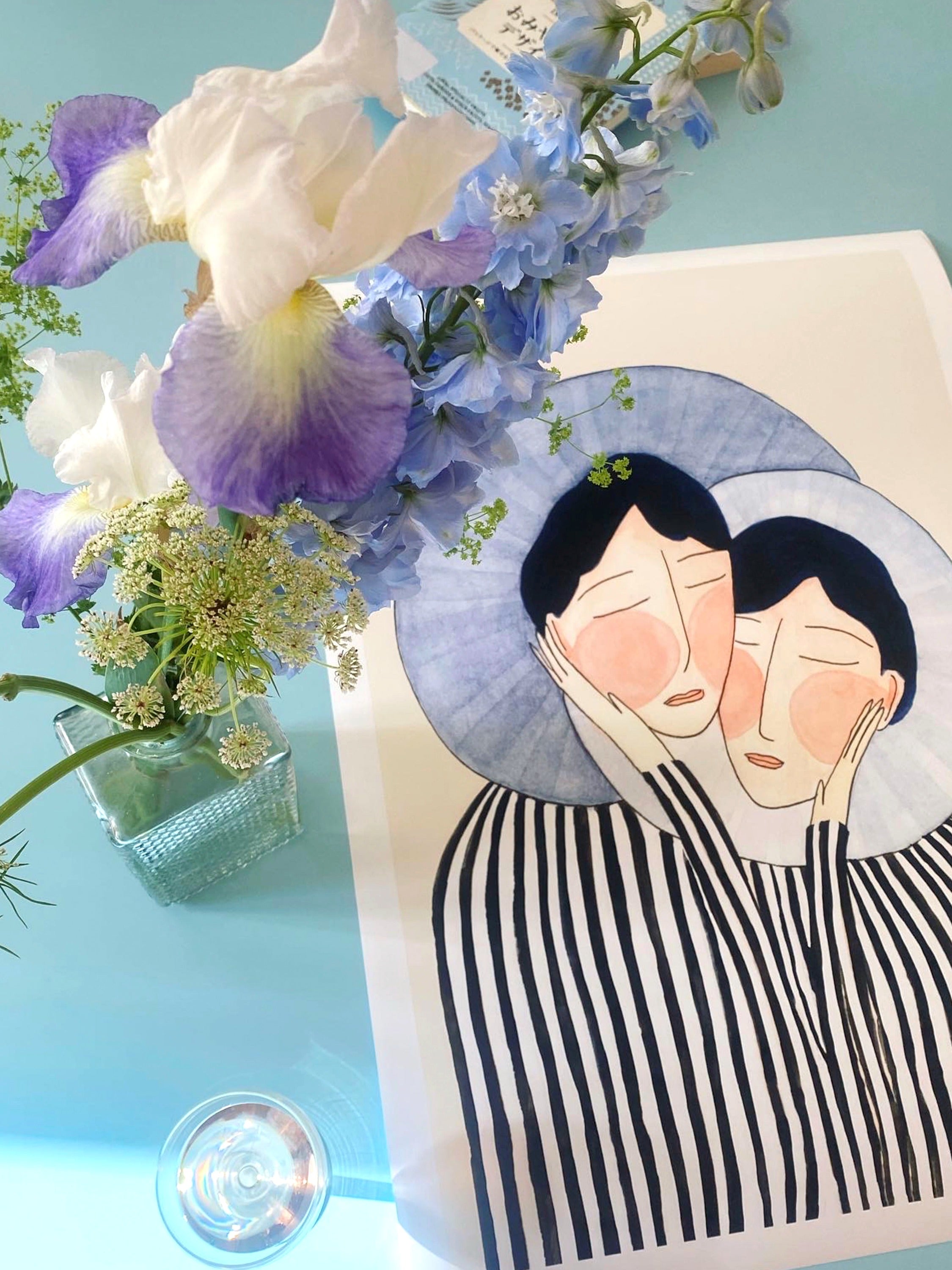 SENTIMENTAL BLUES kunstplakat liggende på lyseblåt bord ved buket med blå og hvide iris
