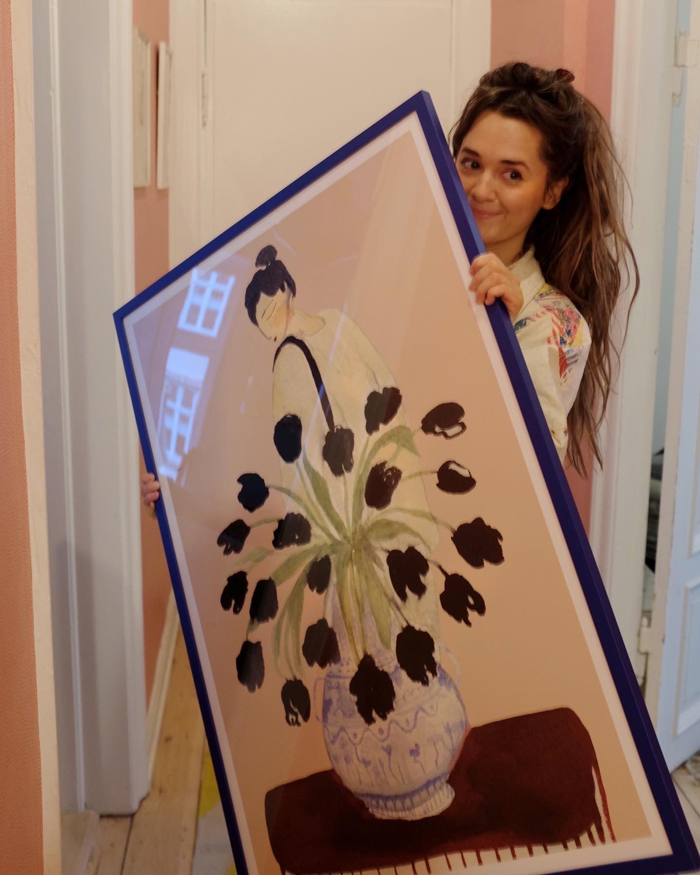 Person holder SUNDAY MARKET kunstplakat med sorte blomster i blå ramme i en gang