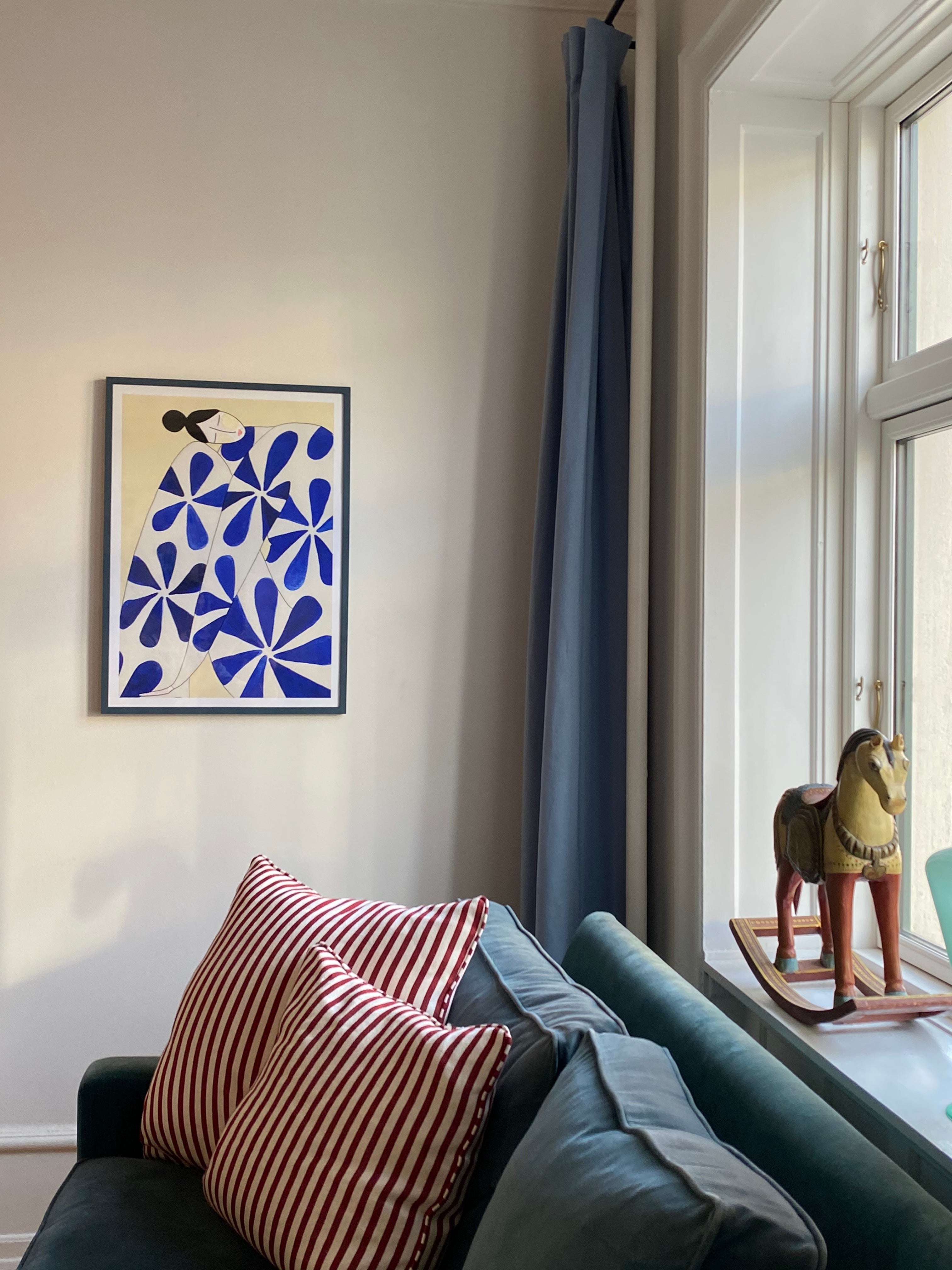 WALLFLOWER kunstplakat i mørk ramme over blå sofa med stribede puder og gyngehest