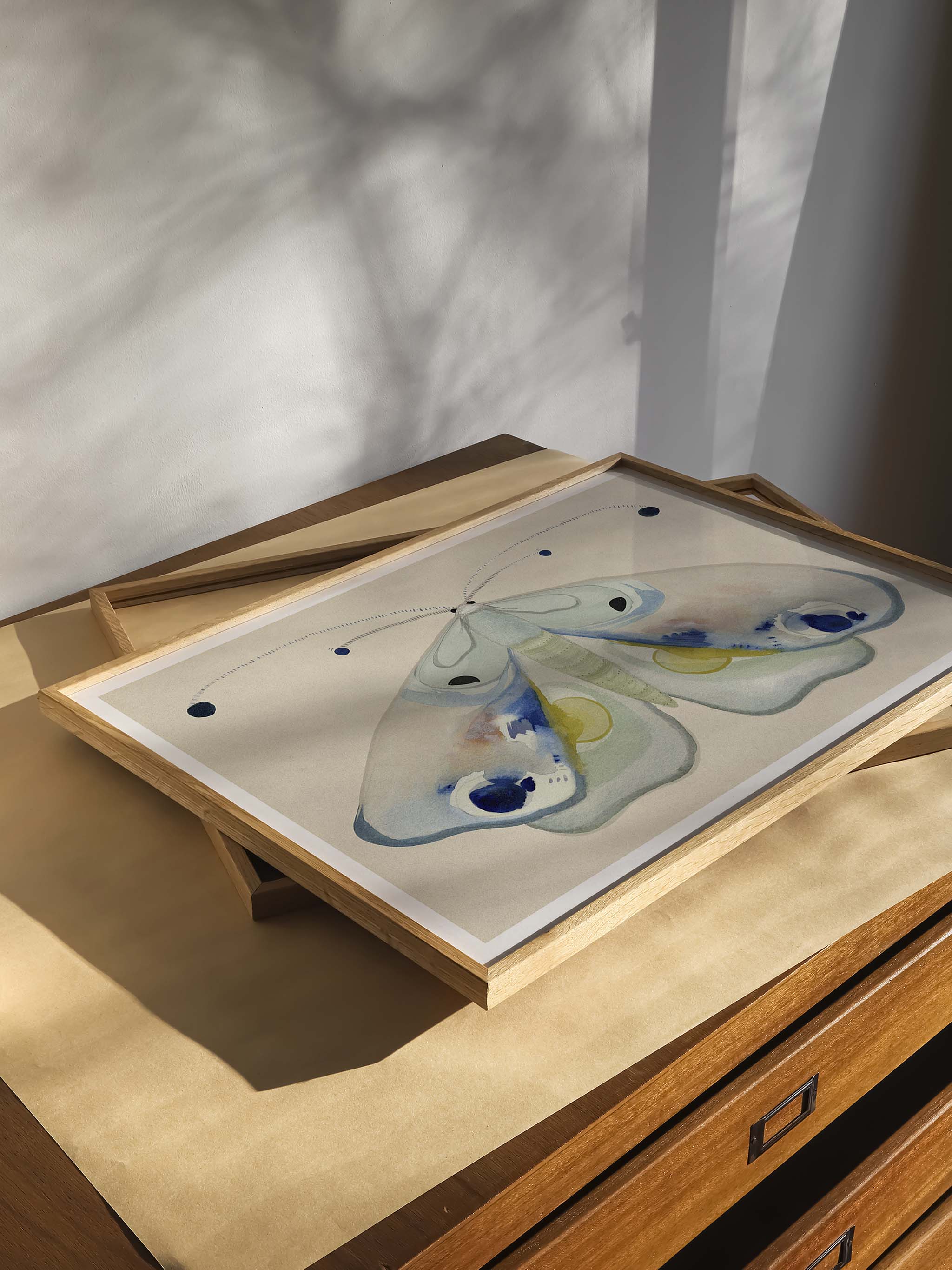 Nærbillede af Natsværmer Dronningen kunstplakat i lys træramme på en kommode