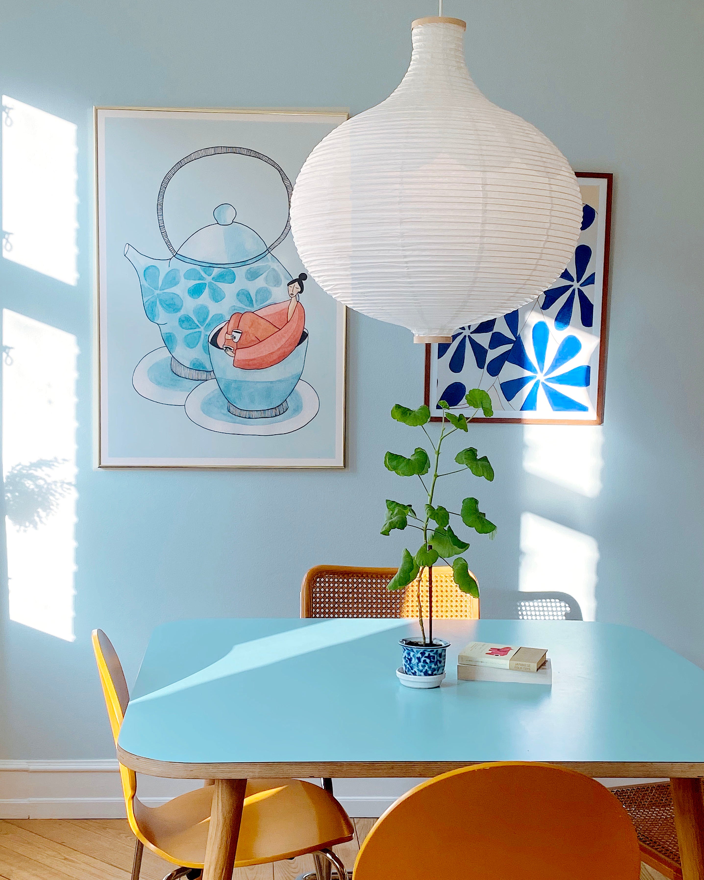 ROOIBOS og WALLFLOWER kunstplakater i lyse rammer over lyseblåt spisebord med papirlampe