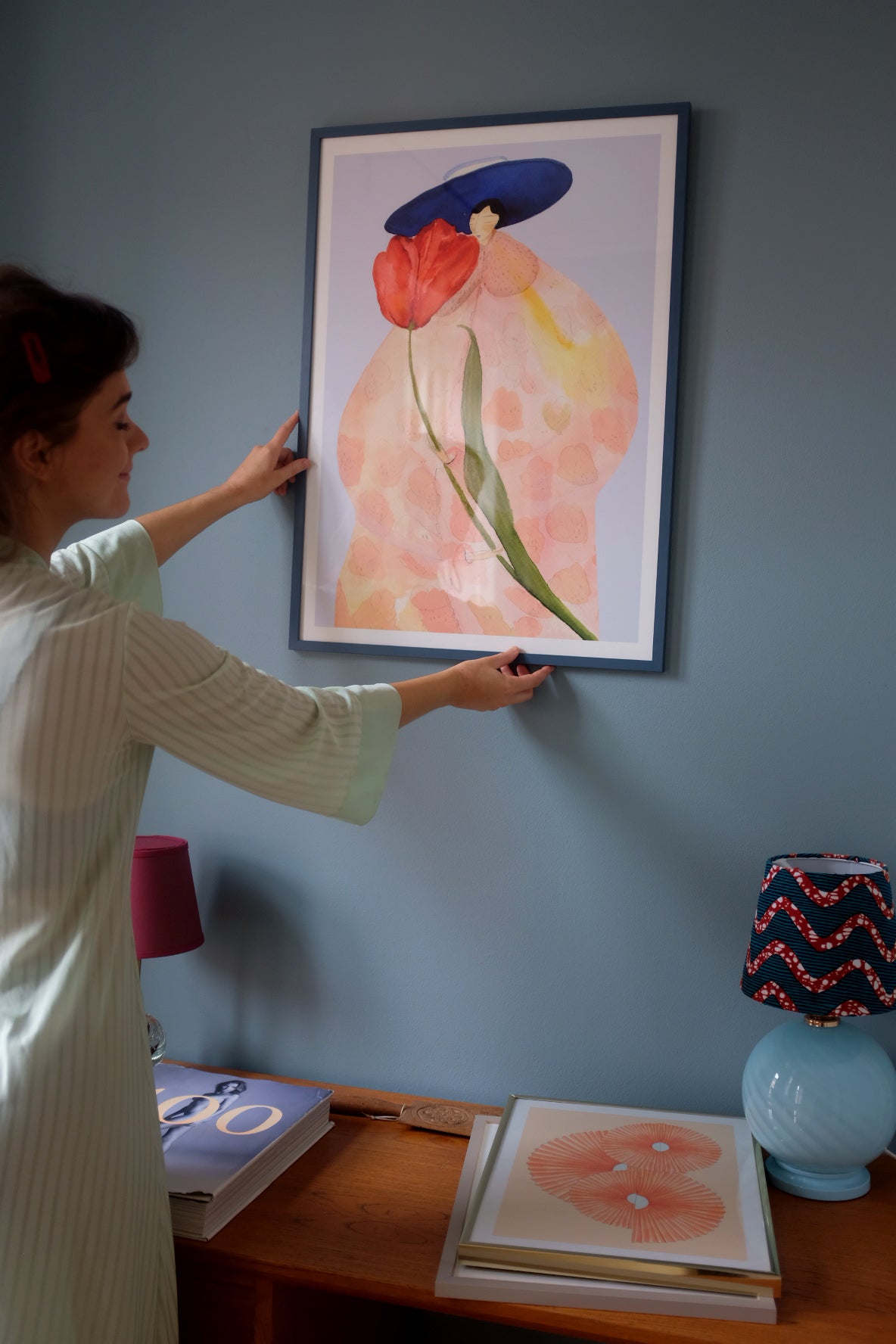Person hænger FRENCH TULIPS kunstplakat op på en blå væg