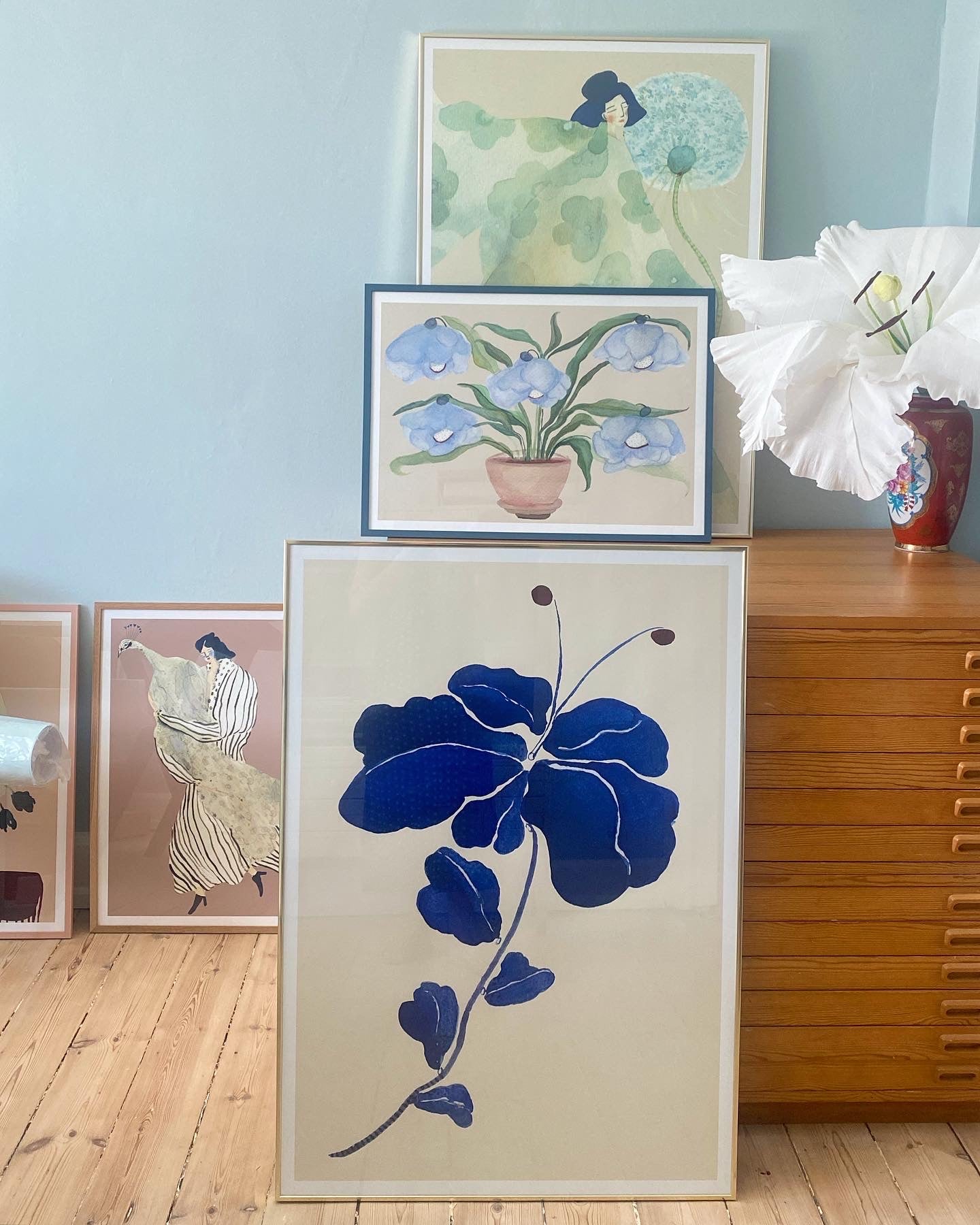 FLEUR DE BLEU kunstplakat med mørkeblå blomst i en billedvæg ved en trækommode